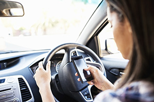 Side view of teenage girl using smart phone while driving car. Horizontal shot.