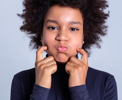 Photo project. Childish curly boy behaving strangely while touching his big inflated cheeks with fingertips