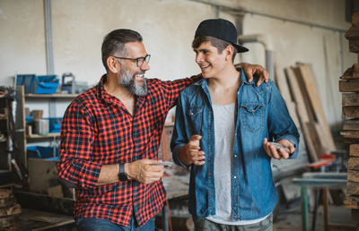 Father and son in carpenter workshop. They are talking about new table they are going to work on, both smiling and satisfied