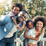 Portrait of a cheerful young mother and father giving their children piggyback rides outside during the day