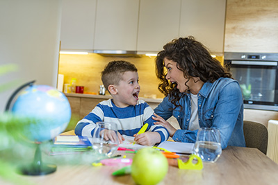 Mom and son are smiling and hugging while doing their homework. Mom helping little boy to do homework. Mom helping kid with homework. Education and family concept