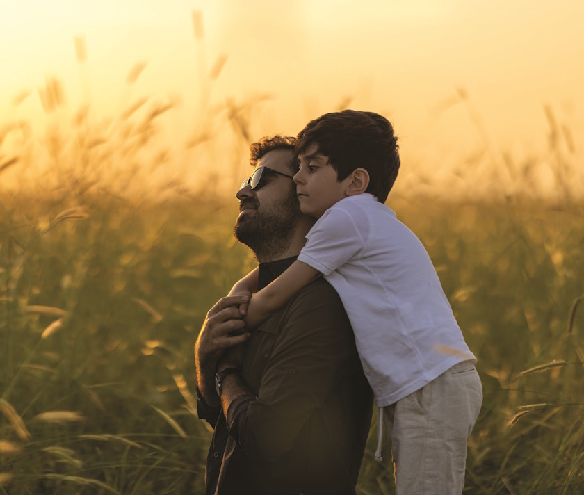Strategies for Dads with ADHD. An image at sunset in a field with a male child wrapping his arms around his father's neck. Dads with ADHD.