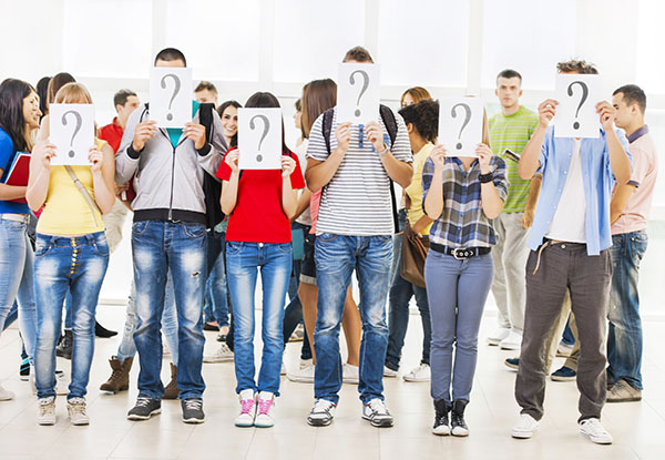 Group of students hiding their faces with question mark sign. Other students are in the background.